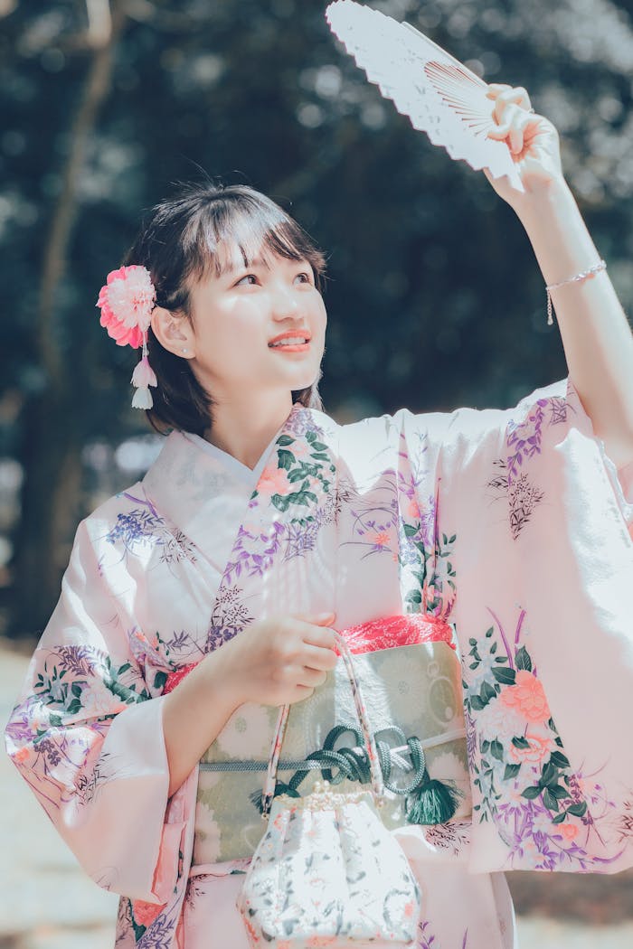 A woman in a floral kimono holds a traditional fan outdoors, exuding grace and cultural elegance.