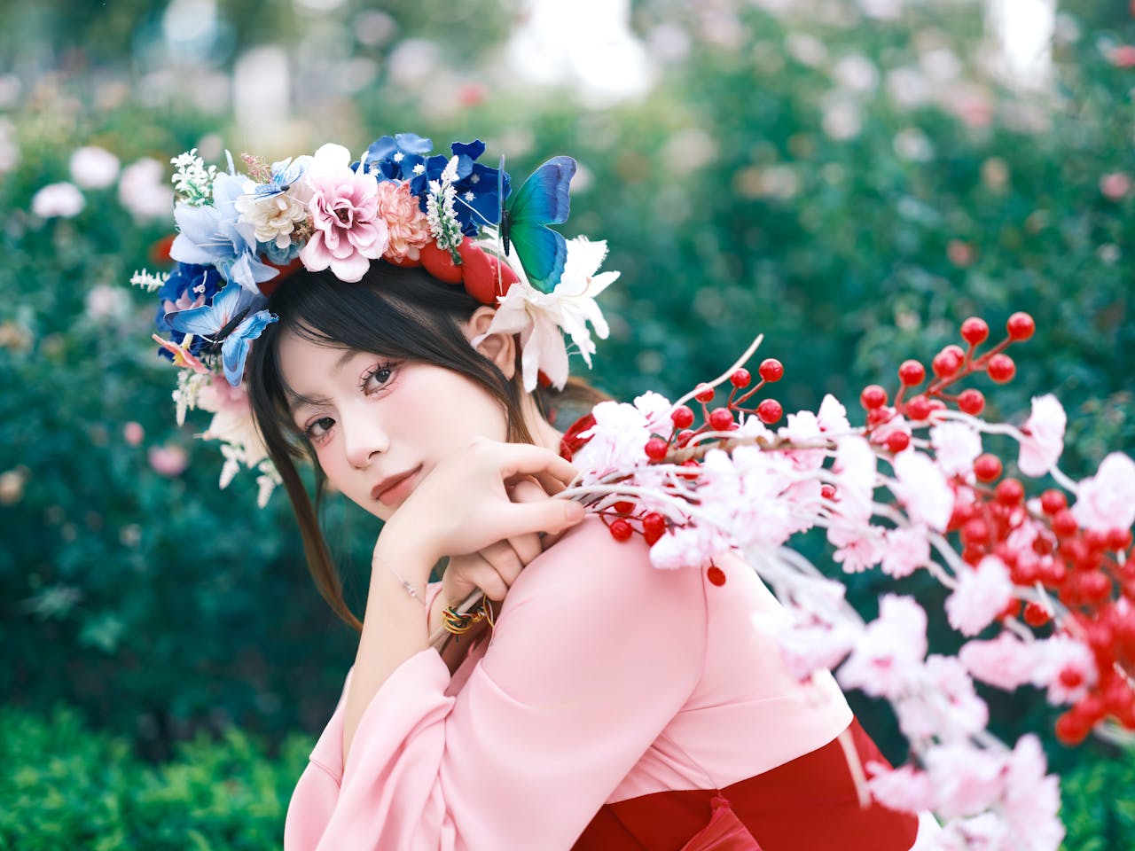Woman in floral headpiece posing outdoors amidst colorful blossoms.
